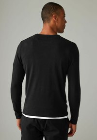 Sort strikket sweater med lange ærmer, rund halsudskæring og en glat tekstur. Har en let tætsiddende silhuet og ribbede kanter.