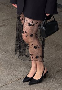 Melni dani legingi ar ziedu izšuvumu, saskaņoti ar melnu sandali. Akcesuāri ietver mazu taisnstūra melnu rokassomu.