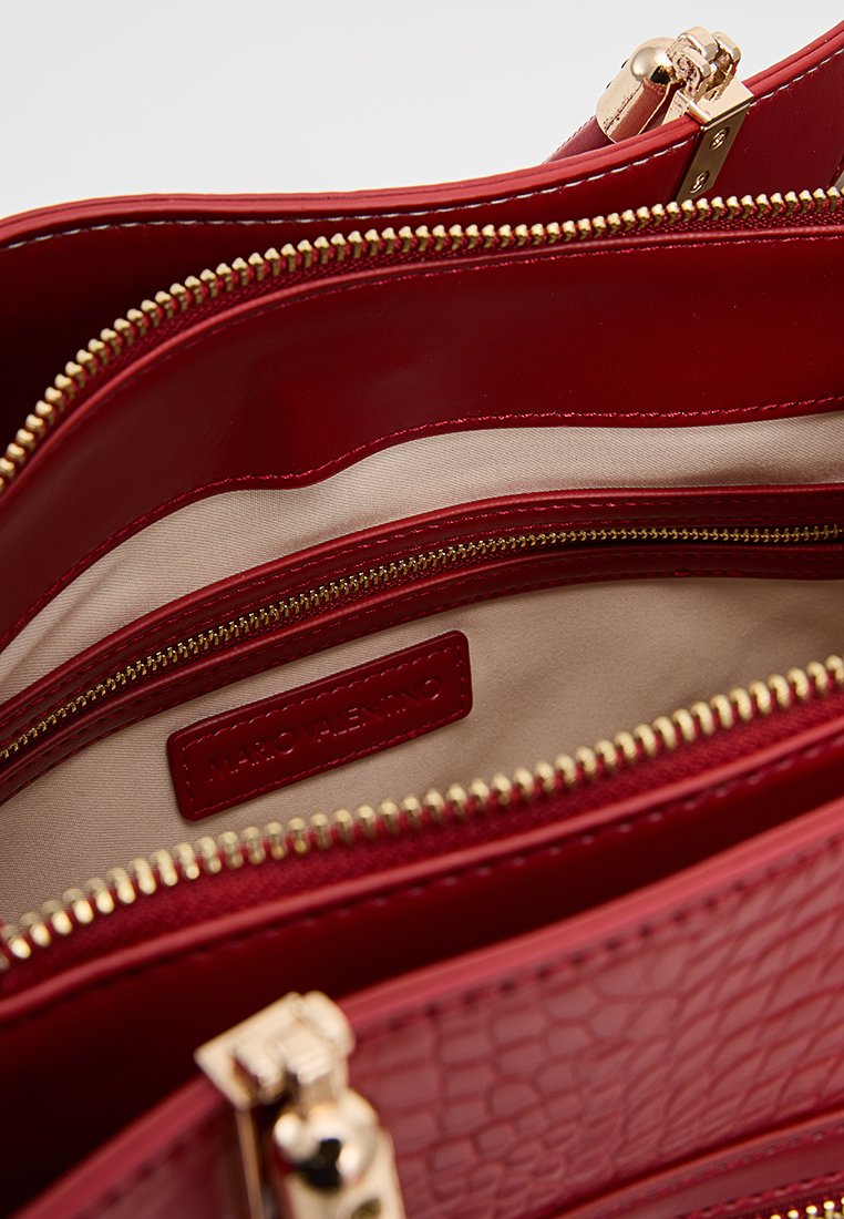La borsa a tracolla in pelle rossa lucida presenta un interno con più scomparti dotati di cerniere dorate. La fodera liscia beige esalta il rivestimento esterno in rosso testurizzato.