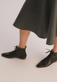 Juodos odinės aulinės botai su smaigalio formos pirštais, raišteliais ir mažu kulnu. Lygus paviršius su subtiliais siuvinėjimo akcentais.