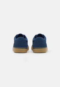 Pair of navy blue sneakers with tan rubber soles viewed from the back on a white background.