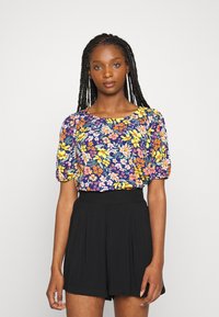 Blusa floral em azul marinho com flores amarelas, rosas e brancas; mangas curtas bufantes; decote redondo. Calções pretos de cintura alta. Textura suave.