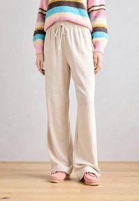 Pantaloni largi de culoare bej deschis, cu talie elastică și șnur. Textura pare moale, completată de încălțăminte roz.
