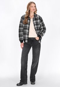 Fekete-fehér kockás zakó laza szabással, fekete bordás mandzsettákkal és egyszínű bézs felsővel, sötét, laza farmerral párosítva.