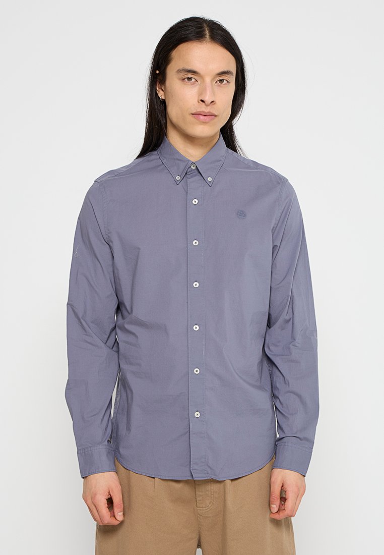 Camisa de botones de manga larga en tejido gris claro, con cuello, placket frontal y detalle sutil de logo en el pecho.
