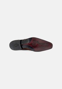 Suela de zapato de cuero marrón con un acabado suave y pulido. Cuenta con un tacón de goma negra y tachuelas decorativas de color dorado.