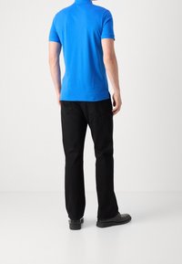 Modrá bavlněná polo tričko v kombinaci s černými kalhotami. Tričko má krátké rukávy a límeček; kalhoty mají rovný střih a zadní kapsy.