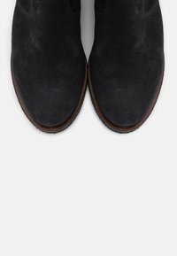 Svarta mocka ankelstövlar med en slät yta, rund tå och en brun gummisula. Inga synliga detaljer eller m önster.