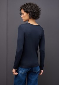 Top a maniche lunghe blu navy realizzato in materiale morbido, presenta un collo a giro e un design aderente, si abbina a pantaloni in denim blu.