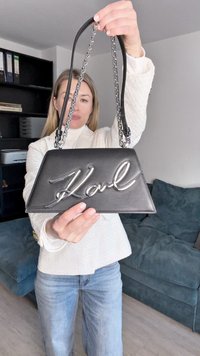 Svart skinnveske med trekantet form og sølvfarget kjedehåndtak. Har en markant metallisk "Karl"-logo på forsiden.