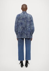 Blå denimjakke med blomsterdesign, lange ermer og knappehals, kombinert med blå vide jeans og ankelstøvler.