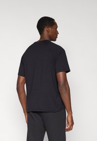 Μαύρο κοντομάνικο t-shirt με στρογγυλή λαιμόκοψη και μανίκια ράγκλαν, φτιαγμένο από μαλακό βαμβακερό ύφασμα με λεία υφή.