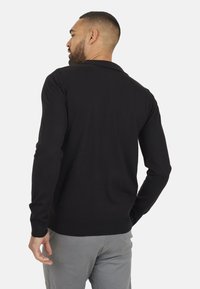 Zwart gebreide cardigan met een geribde kraag, lange mouwen en een aansluitende pasvorm. Beschikt over een gladde textuur en geen zichtbare patronen of logo's.