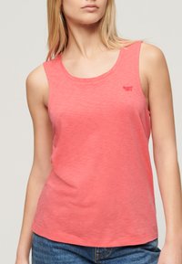 Top sin mangas de color coral hecho de una tela suave, con un escote redondo y un pequeño logo en el área del pecho izquierdo. Corte casual y textura suave.