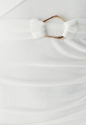 Witte stoffen jurk met een knoopceintuur met een gouden metalen accent. Het materiaal heeft een zachte, getextureerde afwerking met subtiele plooien.