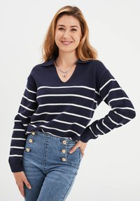 Marineblauwe en witte gestreepte gebreide trui met een V-hals, voorzien van lange mouwen en ribgebreide boorden. Combi met hoog-waist blauwe jeans met knoopaccenten.