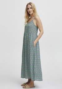 Robe maxi en imprimé floral bleu et vert, avec une coupe décontractée, des bretelles spaghetti et des poches latérales. Tissu léger et design fluide.