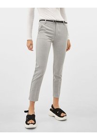 Pantalon gris ajusté à la coupe slim avec passants de ceinture, présentant un motif discret et des fentes sur l'ourlet. Assorti avec des sandales noires.