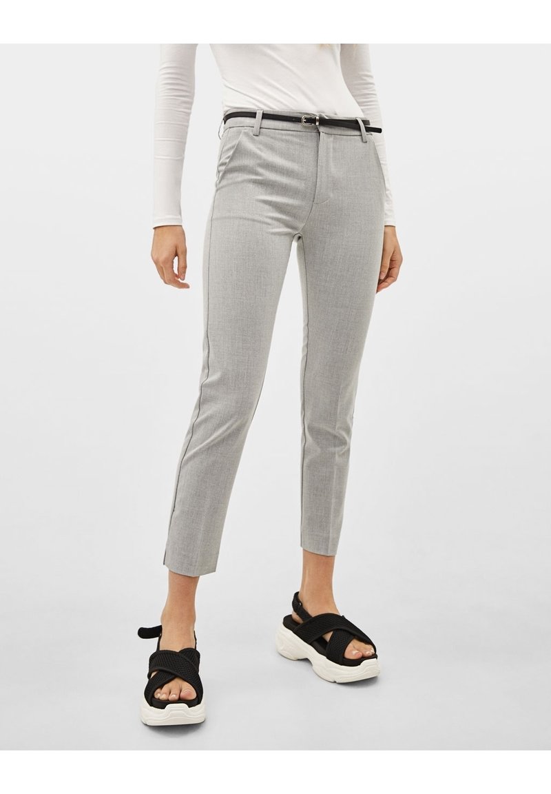 Pantalon gris ajusté à la coupe slim avec passants de ceinture, présentant un motif discret et des fentes sur l'ourlet. Assorti avec des sandales noires.