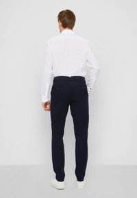 Herrnavybyxor, slim fit, i bomullsblandning, med subtila bakfickor och platt framdesign, i kombination med en vit långärmad skjorta.