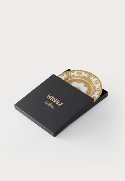 Černá krabička Versace částečně otevřená, uvnitř odhalující bílý a zlatý dekorativní talíř s ozdobným vzorem.