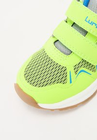 Pantof de sport vibrant, de culoare verde neon, cu panouri din plasă, accente albastre și trei bretele ajustabile cu Velcro. Talpa din cauciuc oferă aderență.