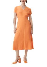 Pomarańczowa midi sukienka z dekoltem w serek i krótkimi rękawami, wykonana z lekkiego materiału. W zestawie z błyszczącymi pomarańczowymi butami na słupku.