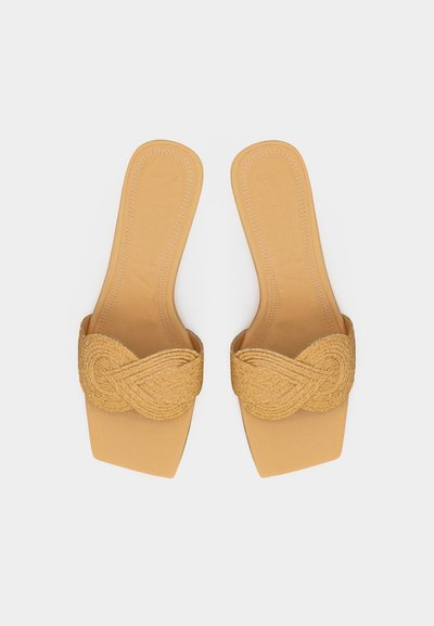 Barna csúszásmentes szandálok négyzet alakú orral és fonott pántokkal az elején, felülről nézve, sima háttér előtt.