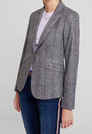 Blazer grigio a righe con accenti rosa, tessuto testurizzato, chiusura a singolo bottone e rever a falda. Abbinato a jeans blu con righe laterali.