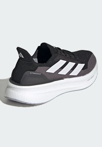 Sneaker atletico nero e grigio con una tomaia testurizzata, branding a tre strisce bianche e una spessa suola bianca con dettagli "LIGHTBOOST".