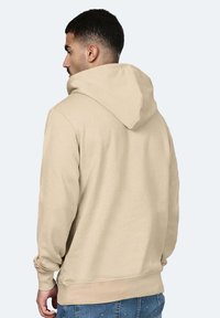 Felpa con cappuccio beige dal tessuto morbido, con tasca a marsupio e polsini a coste, mostrata da dietro con una vestibilità rilassata.