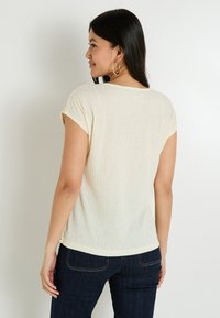 Top de manga corta color crema con un acabado texturizado, escote redondo y corte relajado, combinado con jeans de mezclilla oscuros.