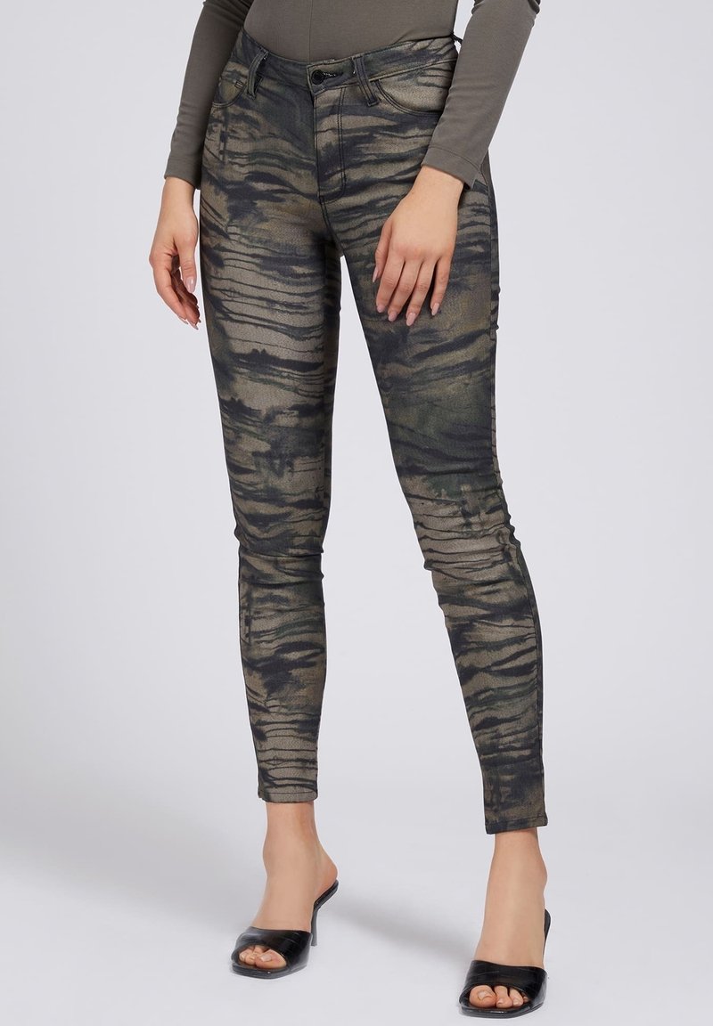 Pantalon slim à motif rayures tigre vert foncé et noir, porté avec un haut à manches longues et des talons noirs ouverts.