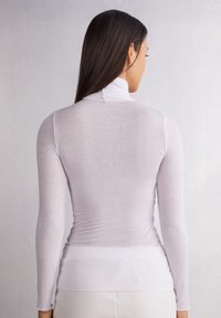 Vit långärmad turtleneck-topp med en åtsittande design, ribbad textur och ett mjukt, lätt tyg, sedd bakifrån.
