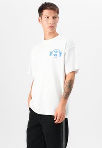 White cotton t-shirt featuring a blue graphic design with headphones and a logo on the chest, paired with black denim pants.