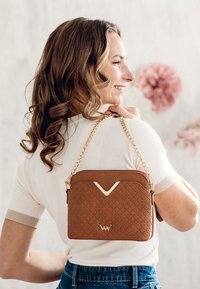 Brown quilted leather handbag with a gold chain strap, featuring a v-shaped accent and a logo detail at the bottom. Compact rectangular shape.