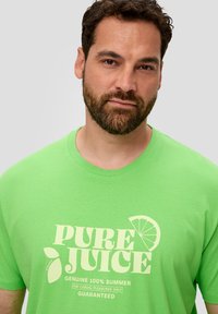 Grünes Baumwoll-T-Shirt mit Rundhalsausschnitt, das den Text "PURE JUICE" und eine Limette-Grafik zeigt. Weicher Stoff, lässige Passform.