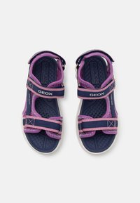 Lilla og marine sandaler med justerbare stropper, teksturerte såler og hvite gummiyttersåler. Har Geox-logo og akcent-innsnitt.