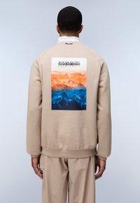 Sudadera beige con un gráfico rectangular que muestra un paisaje montañoso en tonos naranja y azul en la parte posterior. Puños y dobladillo acanalados.