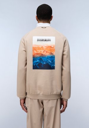 Il pullover beige presenta una grafica rettangolare che rappresenta un paesaggio montano arancione e blu sul retro. Maniche e orlo a coste.