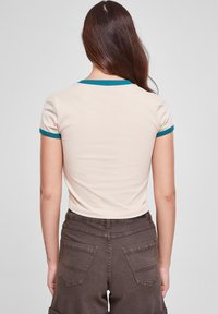 Beige cropped t-shirt with teal ribbed collar and sleeve accents. Soft material with a fitted design, paired with dark brown pants featuring pockets.