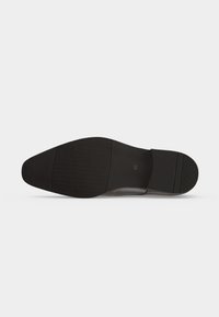 Semelle de chaussure de ville en cuir noir avec grip texturé et numéro de taille 42 estampillé près du talon sur fond blanc.