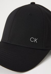 Μαύρο καπέλο μπέιζμπολ κατασκευασμένο από υφασμάτινο πλέγμα. Διαθέτει καμπύλο γείσο και μικρό κεντημένο λογότυπο "CK" σε ασημί χρώμα στο μπροστινό μέρος.