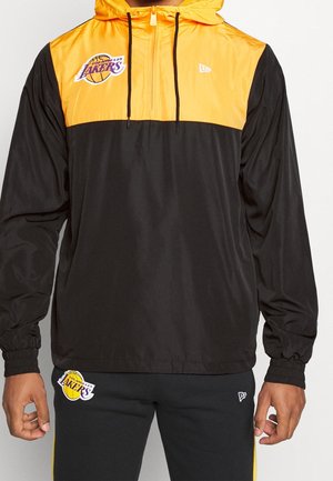 Mann trägt schwarze und gelbe Los Angeles Lakers Jacke mit Kapuze und passende schwarze Hose mit Team-Logos.
