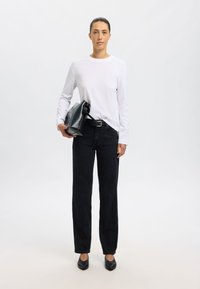 Biały top z długim rękawem, czarne dżinsy o prostym kroju, czarne płaskie buty, trzymający czarną skórzaną torebkę o eleganckim designie z złotymi akcentami.