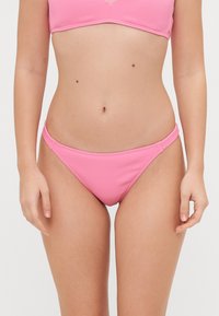 Rožinės juostos formos bikini kelnaitės su žema juosmens linija, plonomis šoninėmis juostelėmis ir lygiu paviršiumi. Paprastas dizainas be papildomų raštų ar akcentų.