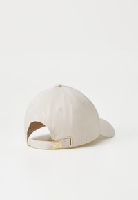 Casquette en coton beige avec une visière courbée et une sangle arrière ajustable avec une boucle en ton doré. Texture lisse et détails cousus.