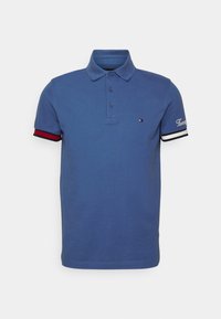 Blå polotröja i bomull med klassisk krage, treknappsstängning och randiga detaljer i röd och vit på ärmarna.