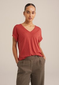 T-shirt rouge à col en V avec des manches courtes retroussées, présentant un motif en losanges texturé, associé à un pantalon taille haute vert olive.