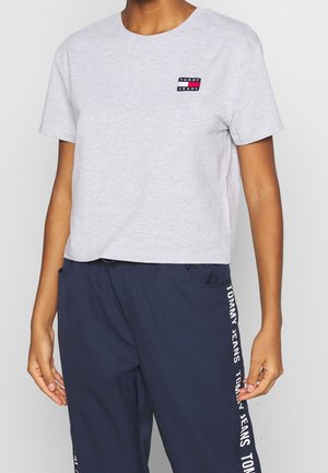 Osoba nosząca jasnoszary krótki t-shirt Tommy Jeans i granatowe spodnie z napisem Tommy Jeans z boku.